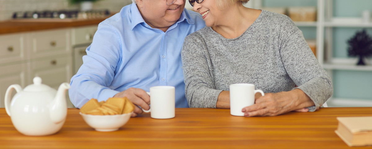 an elder couple together having tea and biscuits in a kitchen
